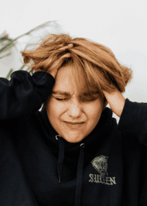 Woman with her face scrunched up and her hands clutching her head due to interruptions in thought processes in adults