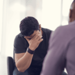 Man sitting across from a therapist with his head in his hands talking about overcompensation in adult relationships