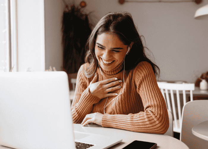 Woman smiling and looking at her laptop, receiving therapy for paranoid thoughts in adults