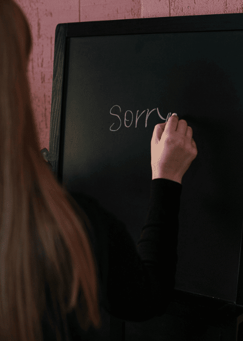 Woman writing sorry on a whiteboard due to struggling with over-apologizing in adults