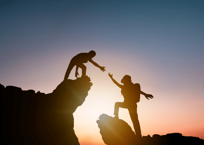 Woman reaching out for help when on the edge of a rock after receiving support for refusal to ask for help in adulthood
