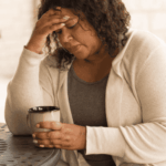 woman sitting at table drinking coffee with hand on head worrying about Sutter health plan mental health coverage