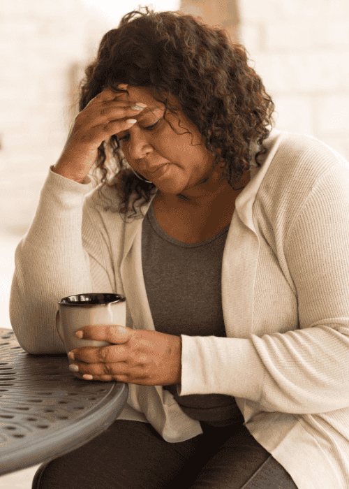 woman sitting at table drinking coffee with hand on head worrying about Sutter health plan mental health coverage