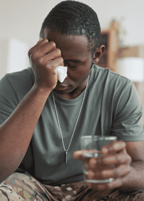 veteran sitting with hand on head holding glass of water worrying about using TRICARE mental health coverage