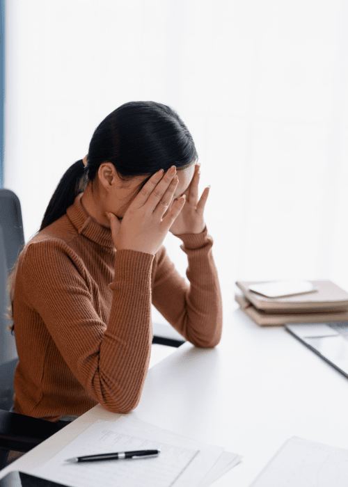 woman at work sitting at desk with hands raised to face experiencing cognitive distortions in adults