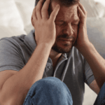 man sitting on floor by sofa with knees up and hands raised to head needing support with most common cognitive distortions in adults