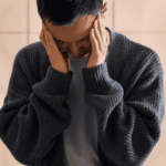 Man standing in kitchen leaning against counter top with hands on head experiencing depression and distorted thinking patterns in adults