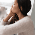 woman sitting by window resting chin on hand, thinking about Kaiser mental health insurance coverage