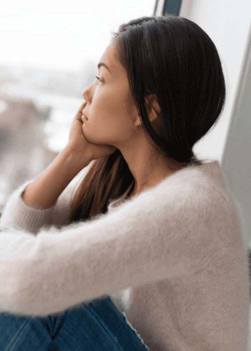 woman sitting by window resting chin on hand, thinking about Kaiser mental health coverage