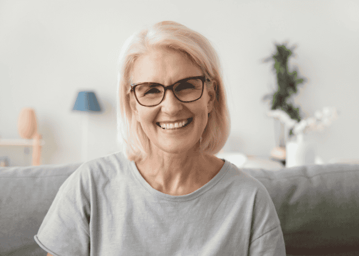 Woman sitting on sofa smiling after receiving support with Employers Health Network (EHN) mental health coverage