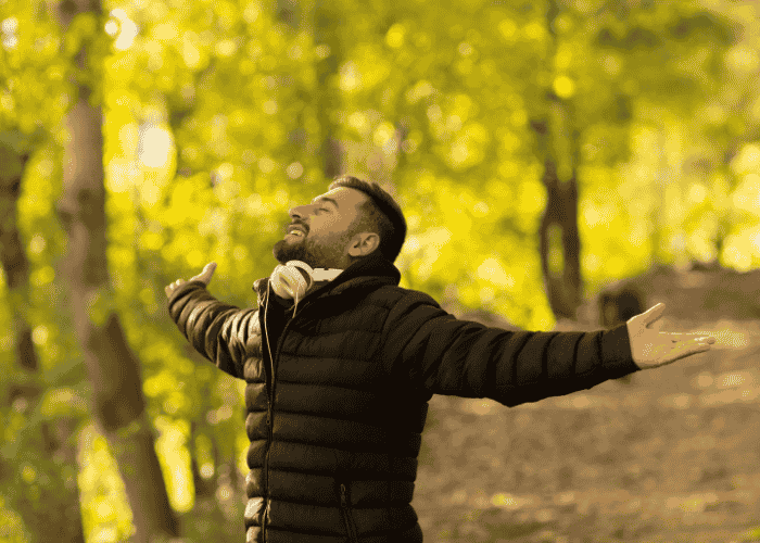man standing in woodland with arms outstretched smiling after support with seeking support with childhood experiences and adult thought patterns