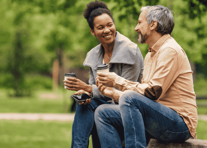 woman sitting with male friend in park drinking coffee smiling after seeking support with Sharp Health Plan mental health insurance coverage