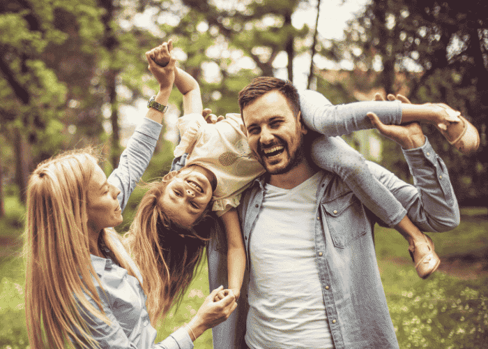 man walking in woodland with wife and carrying young daughter on shoulders smiling after seeking support with Sutter health plan mental health coverage