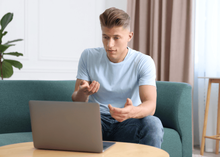 Man sitting on sofa using a laptop for a telehealth call after researching the future of mental health care