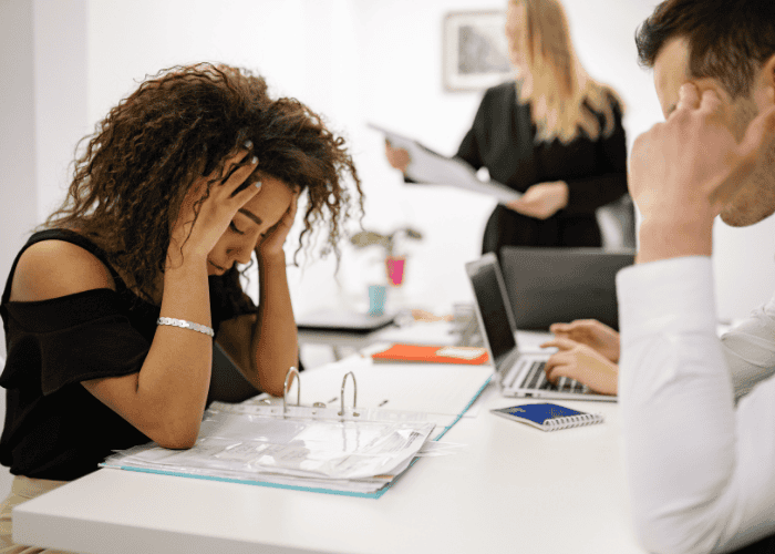 Woman sitting at desk at work with head in hands struggling to achieve a mentally healthy workplace culture