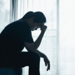 Woman sitting on edge of bed with her hand on her forehead needing information on what to do when mental health coverage is denied in California