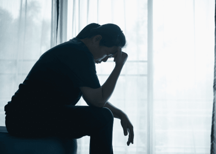 Woman sitting on edge of bed with her hand on her forehead needing information on what to do when mental health coverage is denied in California
