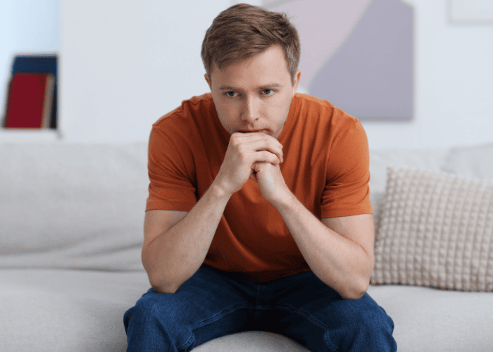 Man sitting on sofa with chin resting on hands worrying about expanded CARE Court eligibility in California