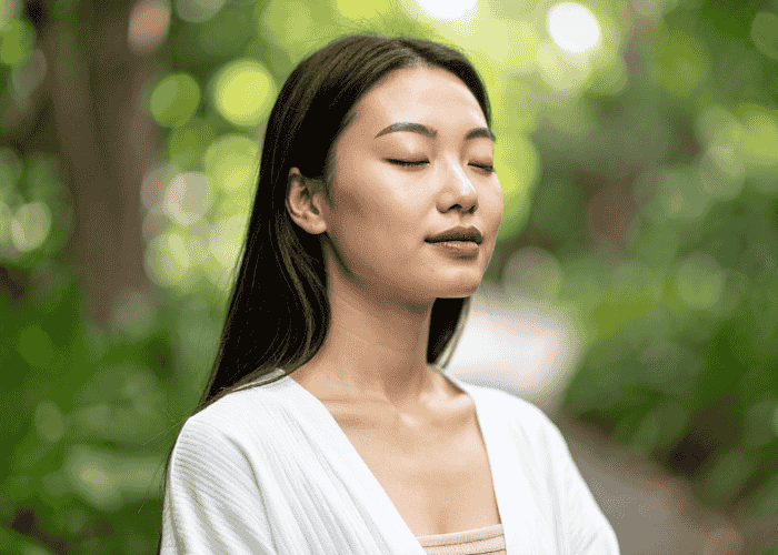 Woman meditating outside in woodland with eyes closed after support with how everyday choices affect your mental health