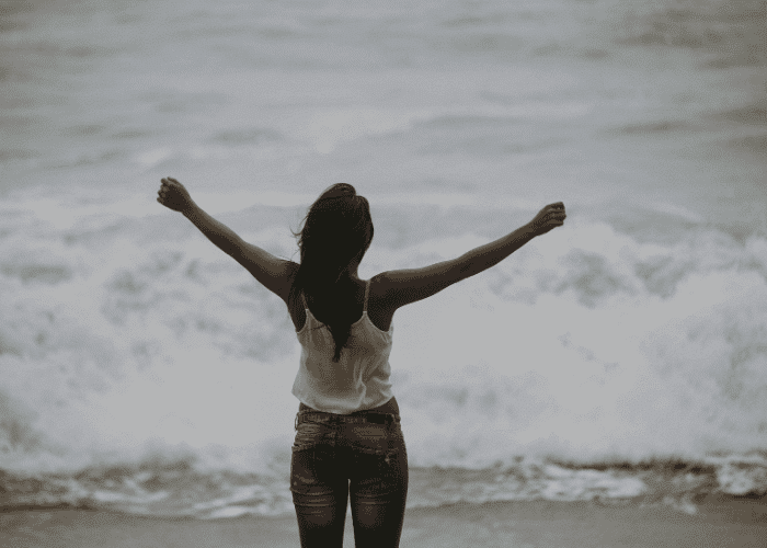 Woman standing in front of the sea with her arms up in victory after receiving treatment for trauma and cognitive distortions
