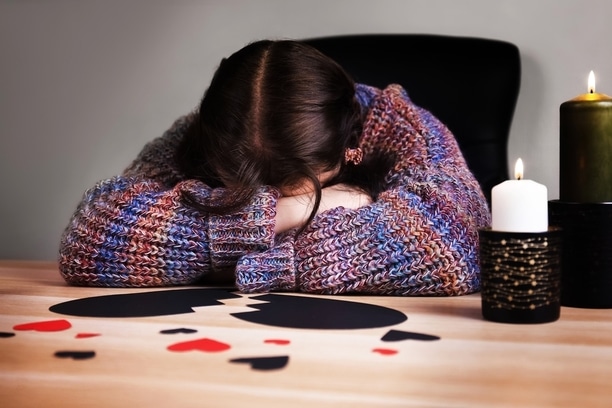 Woman crying into her arms surrounded by paper hearts on a table