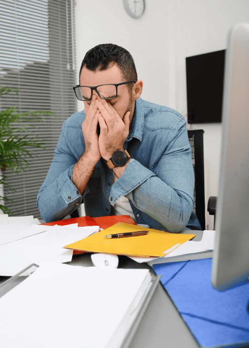 Man with his head in his hands in front of paperwork experiencing burnout vs clinical depression in professionals