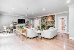 Large bright living room with white sofas and fireplace with decorative stone up the wall