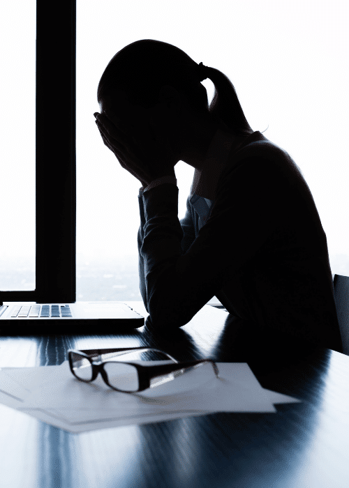 Silhouette of a woman sitting at a desk with her head in her hands needing support from Employee Assistance Programs