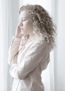Woman looking out of window with hand up to her face worrying about managing mental health treatment while working full-time/