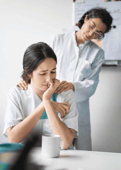 Woman sitting at desk upset at work and colleague wondering how professionals refer patients to outpatient mental health care