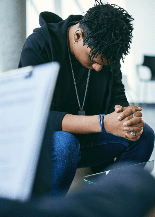 Man sitting on coach with hands together and head down after considering short-term disability for mental health treatment