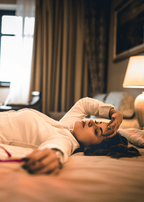 A woman lying on hotel bed wearing work clothes needing support with telehealth access for traveling professionals