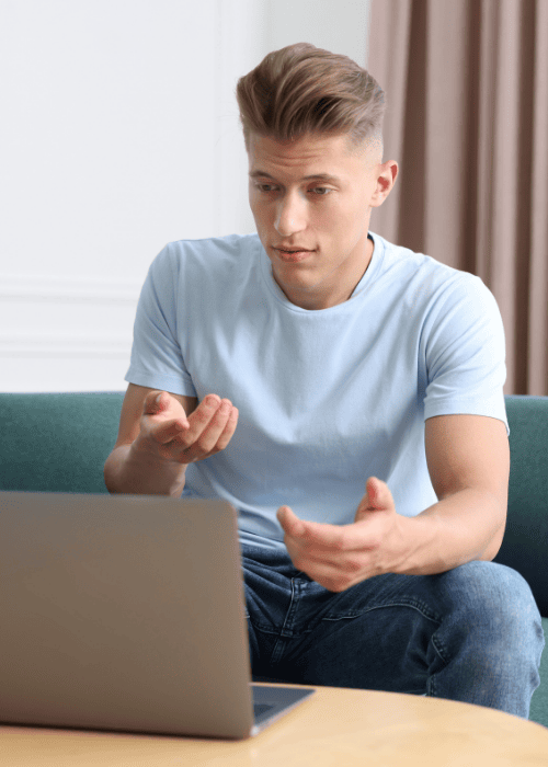 Man sitting on couch using a laptop to access telehealth mental health services for employees