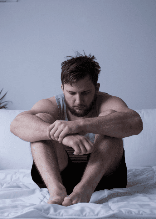 Man sitting on bed with legs drawn towards his chest needing support with fitness-for-duty evaluations