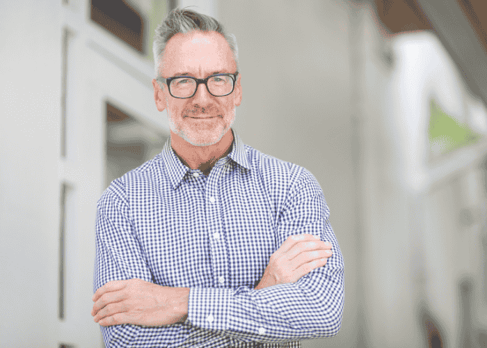 Man standing in office with arms crossed smiling after receiving support with mental health crises in the workplace
