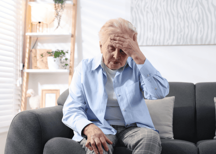 Woman sitting on sofa with hand on head experiencing chronic fatigue syndrome