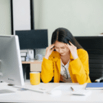 Woman at work sitting at a desk with head in hands needing support with mental health crises in the workplace