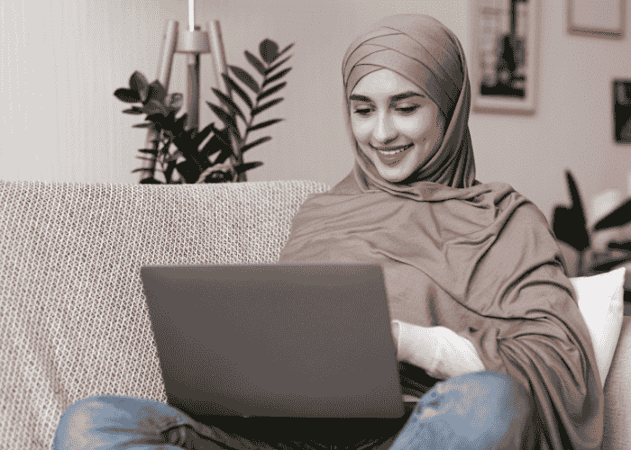 Woman sitting on sofa looking at laptop smiling after receiving support with fitness-for-duty evaluations