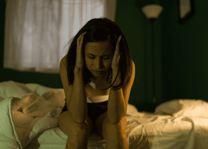 Woman sitting on edge of bed with head in hands needing support with ways to calm anxiety without medication