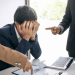 Man in office sitting at desk with colleagues looking over him needing support with how to stop people pleasing