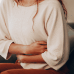 Woman sitting on couch holding stomach in pain needing support with gut health and mental health