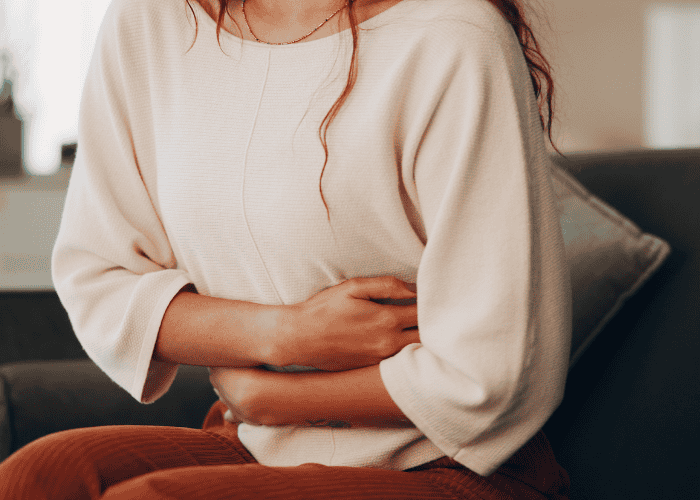 Woman sitting on couch holding stomach in pain needing support with IBS and mental health
