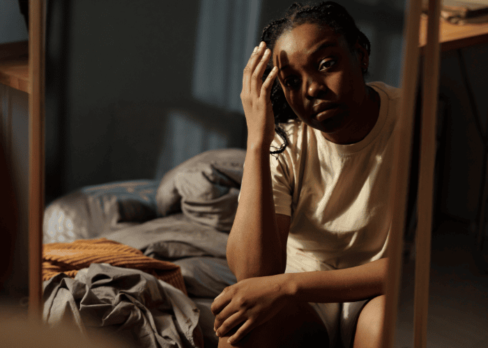 Woman sitting edge of bed with head in hand needing support with gender bias in mental health