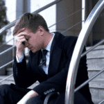 Man sitting outside office on step in suit with head over face experiencing high-functioning depression