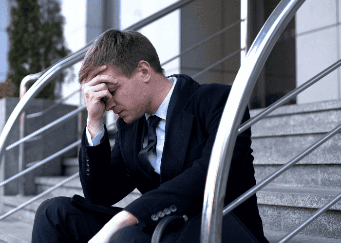 Man sitting outside office on step in suit with head over face experiencing high-functioning depression