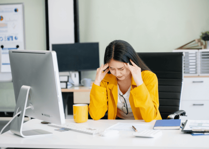 Woman at work sitting at a desk with head in hands needing support with mental health crises in the workplace