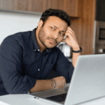 Man sitting at laptop working with head on hand needing support with anxiety awareness