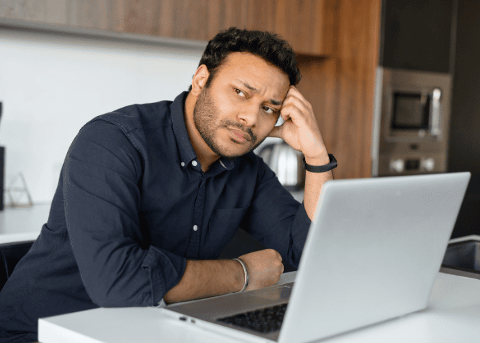 Man sitting at laptop working with head on hand needing support with anxiety awareness