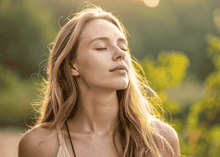 Woman outside with trees behind her with her eyes closed looking calm after support with anxiety awareness