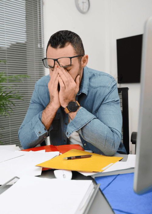 Man sitting at desk covered in paperwork looking overwhelmed and needing support with employer-sponsored mental health benefits